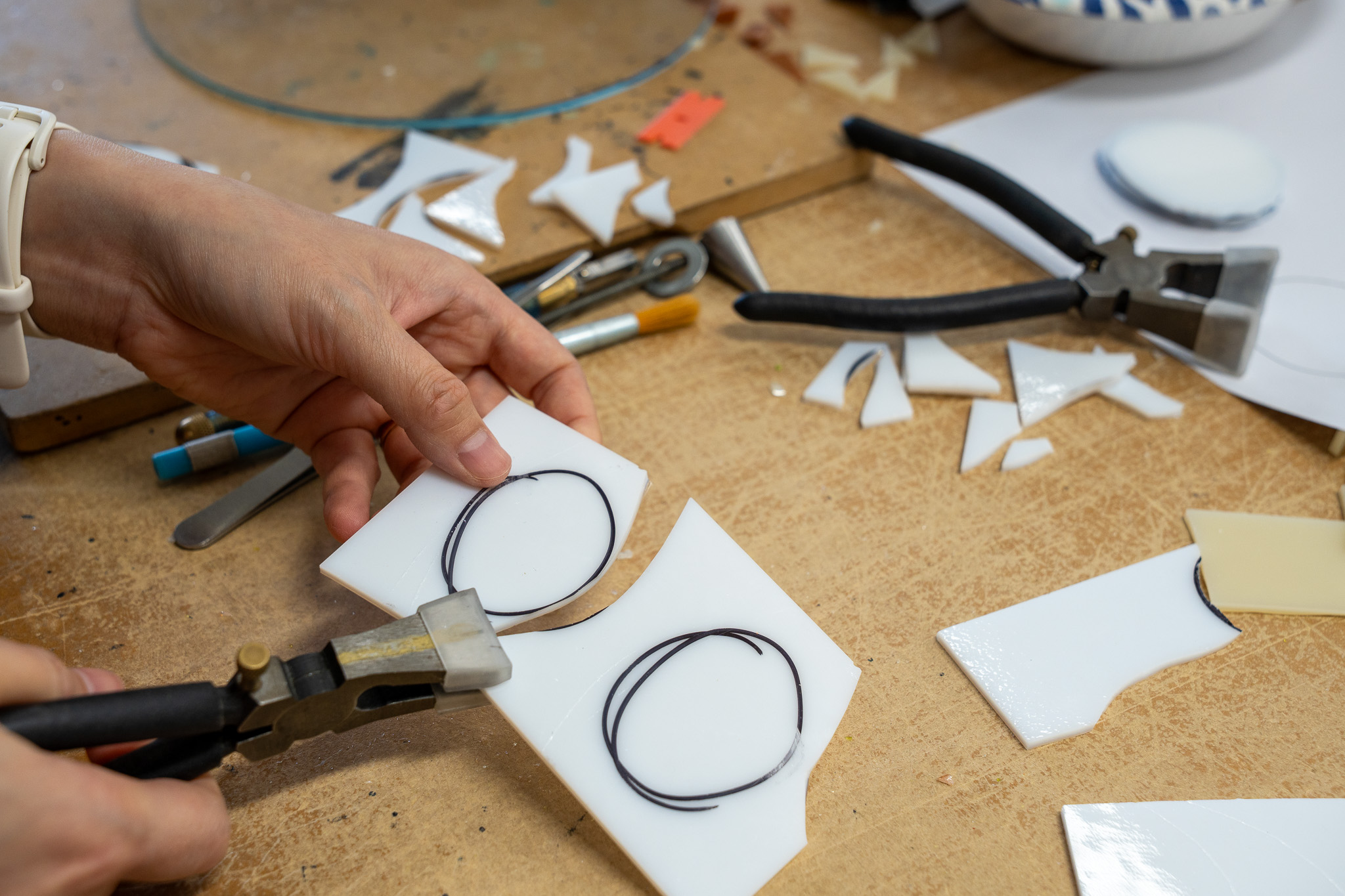 Hands cutting white sheet glass on a studio workbench.