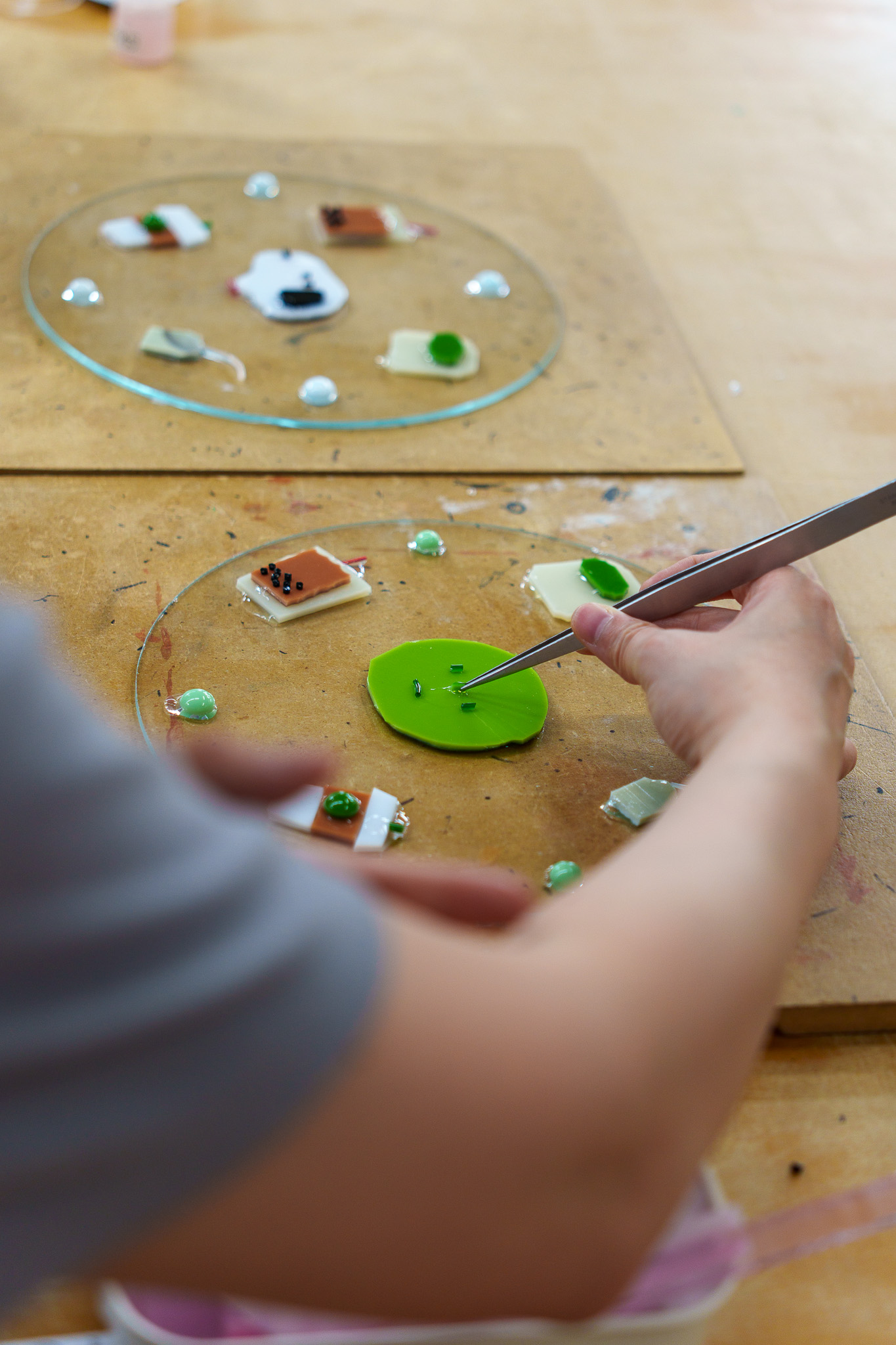 Tweezers placing small green glass details onto a dish composition.